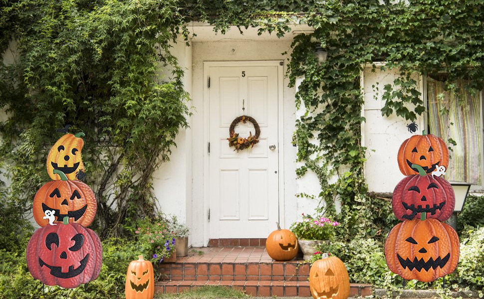 Stacked Halloween pumpkin garden stakes with smiling faces and small ghost and bat ornaments, placed in front of a white door with a wreath.
