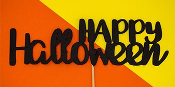Black 'Happy Halloween' cake topper on a stick, set against an orange and yellow background.