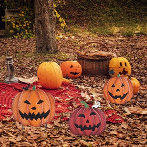 Three stackable metal pumpkin garden stakes with carved faces on a red blanket with real pumpkins and a basket.