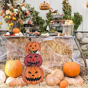 Stackable metal pumpkin garden stakes with hand-painted faces, displayed outdoors with real pumpkins and Halloween decorations.