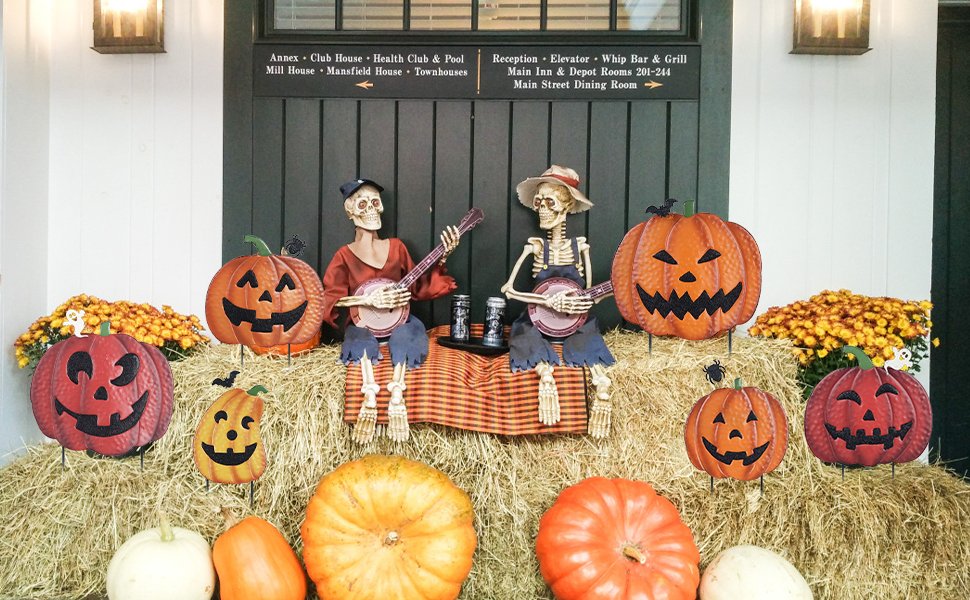 Halloween pumpkin garden stakes and skeleton figures on hay bales with mums and real pumpkins.