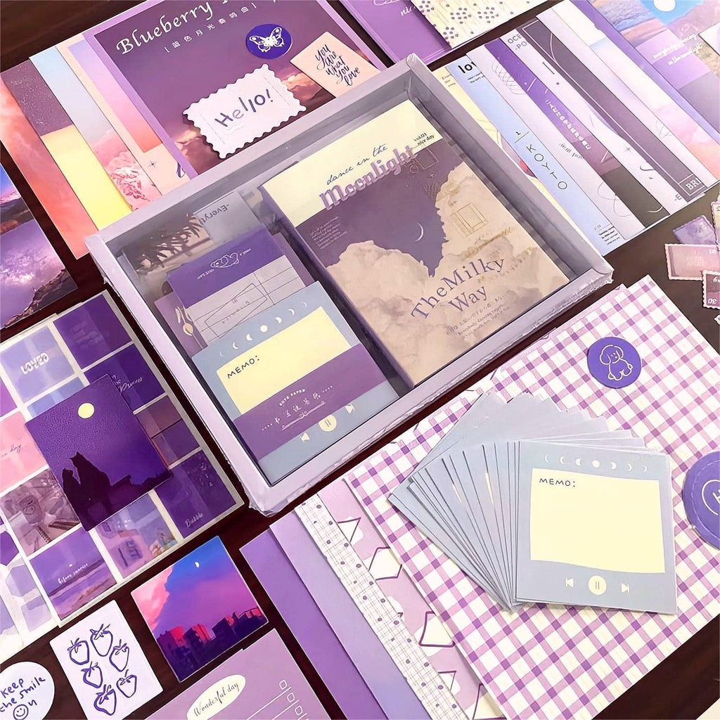 Aesthetic scrapbook kit contents including a grid notebook, stickers, memo pads, and decorative paper in shades of purple.