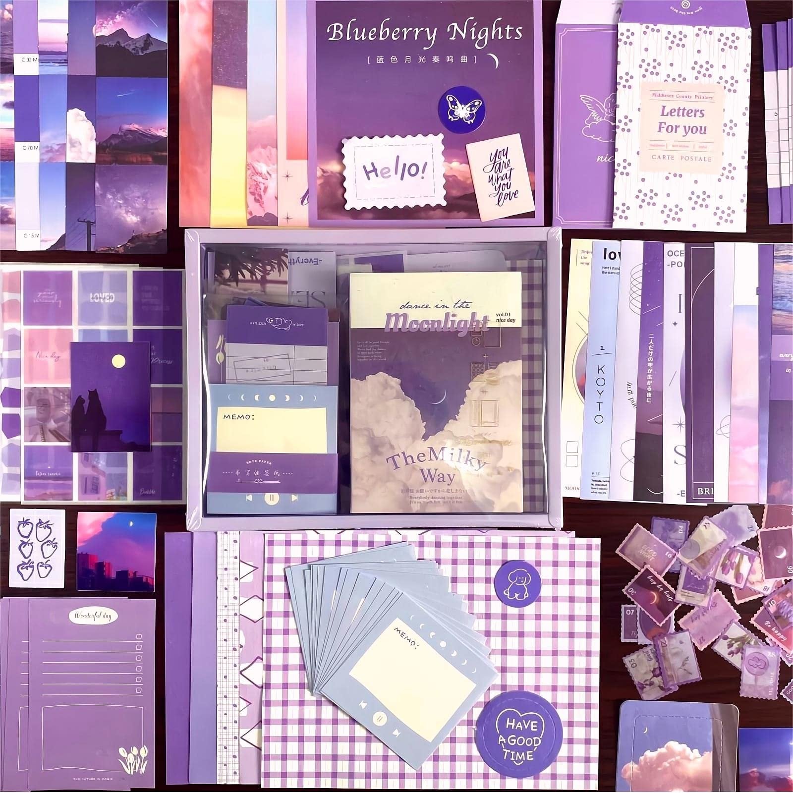 Flat lay of a large aesthetic scrapbook kit with various purple and pink themed papers, stickers, notebooks, and journaling supplies.