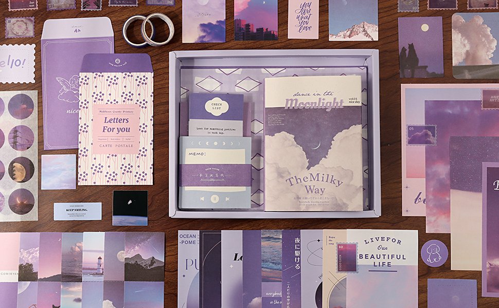 Aesthetic scrapbook kit contents laid out flat, featuring a notebook, stickers, washi tape, and decorative paper in purple and pink tones.