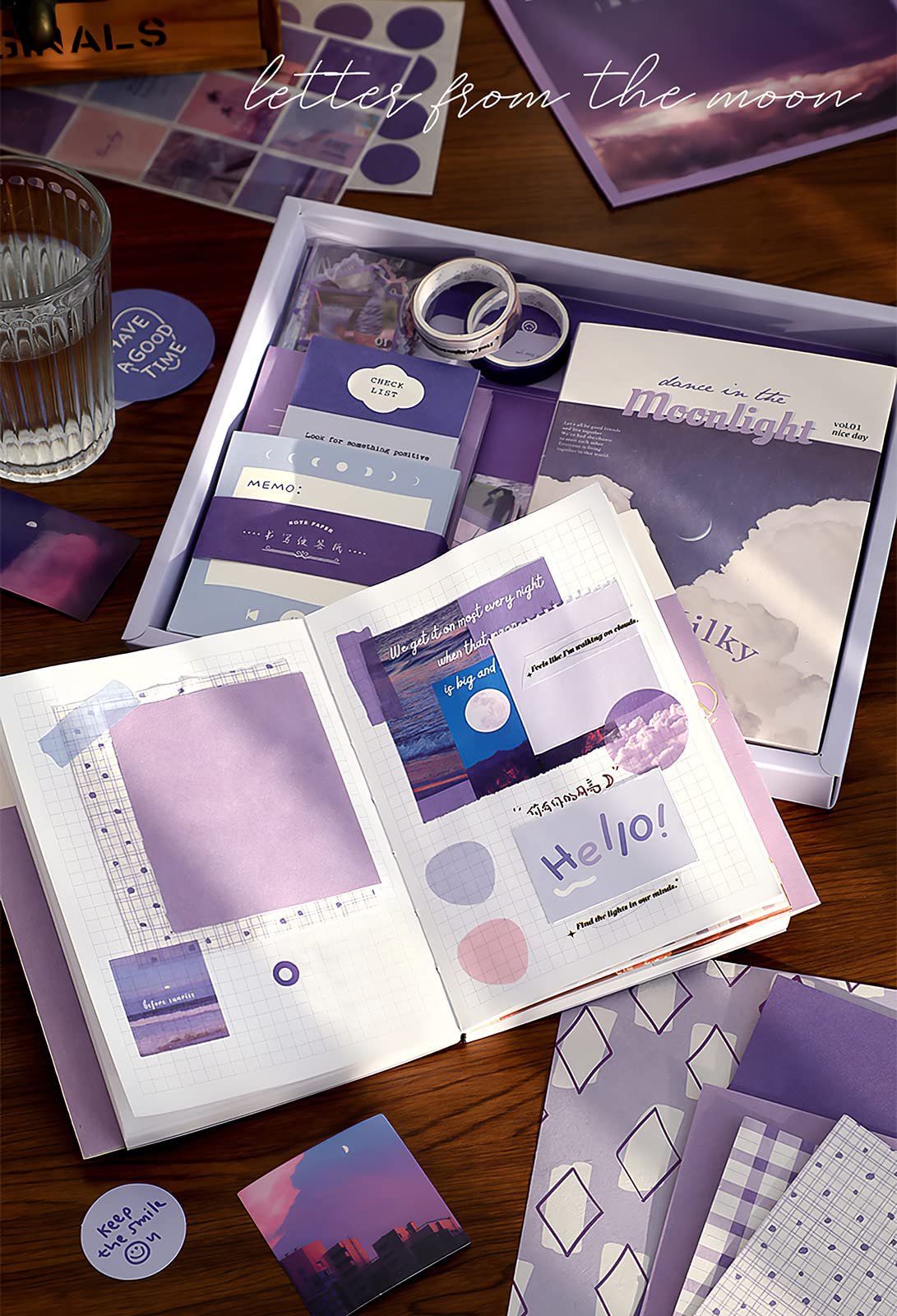 Aesthetic scrapbook kit contents laid out on a wooden table, including a notebook, stickers, washi tape, and decorative paper.