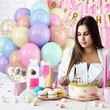 Woman looking at birthday cake with pastel balloons and 'Happy Birthday' banner in background