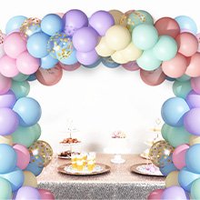 Pastel rainbow balloon arch over a decorated party table with cake and desserts.