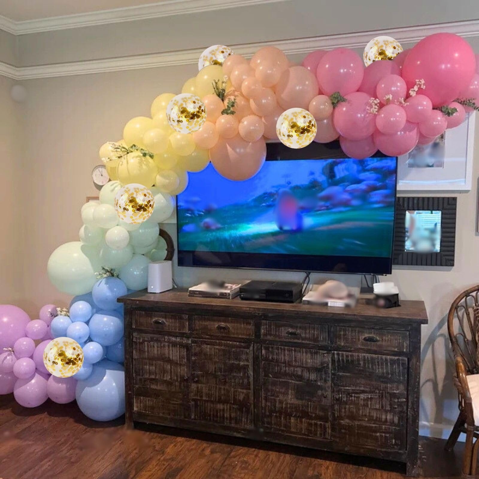 Pastel rainbow balloon arch with gold confetti balloons over a television and wooden cabinet