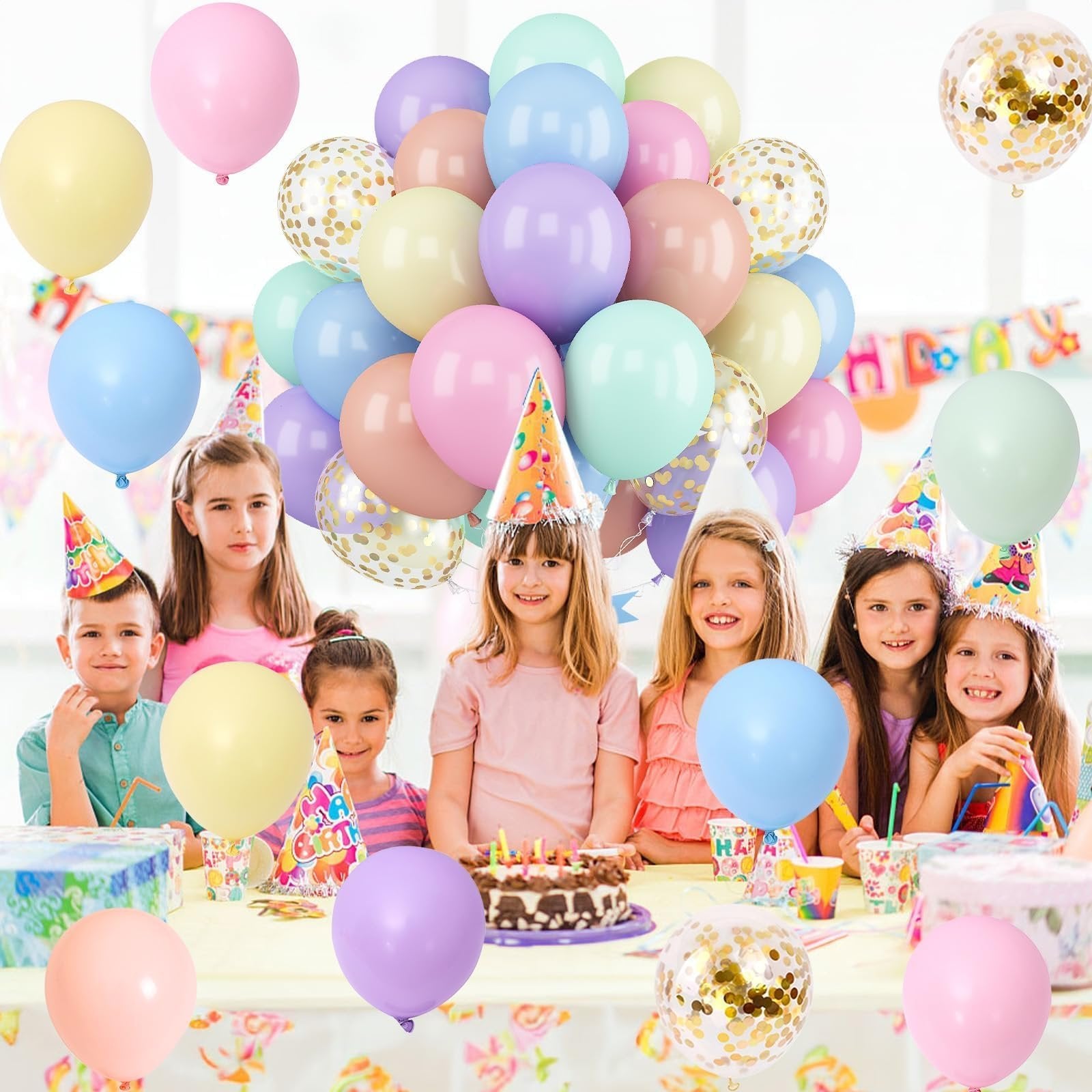 Children wearing party hats at a table with pastel balloons and a birthday cake, celebrating a party.
