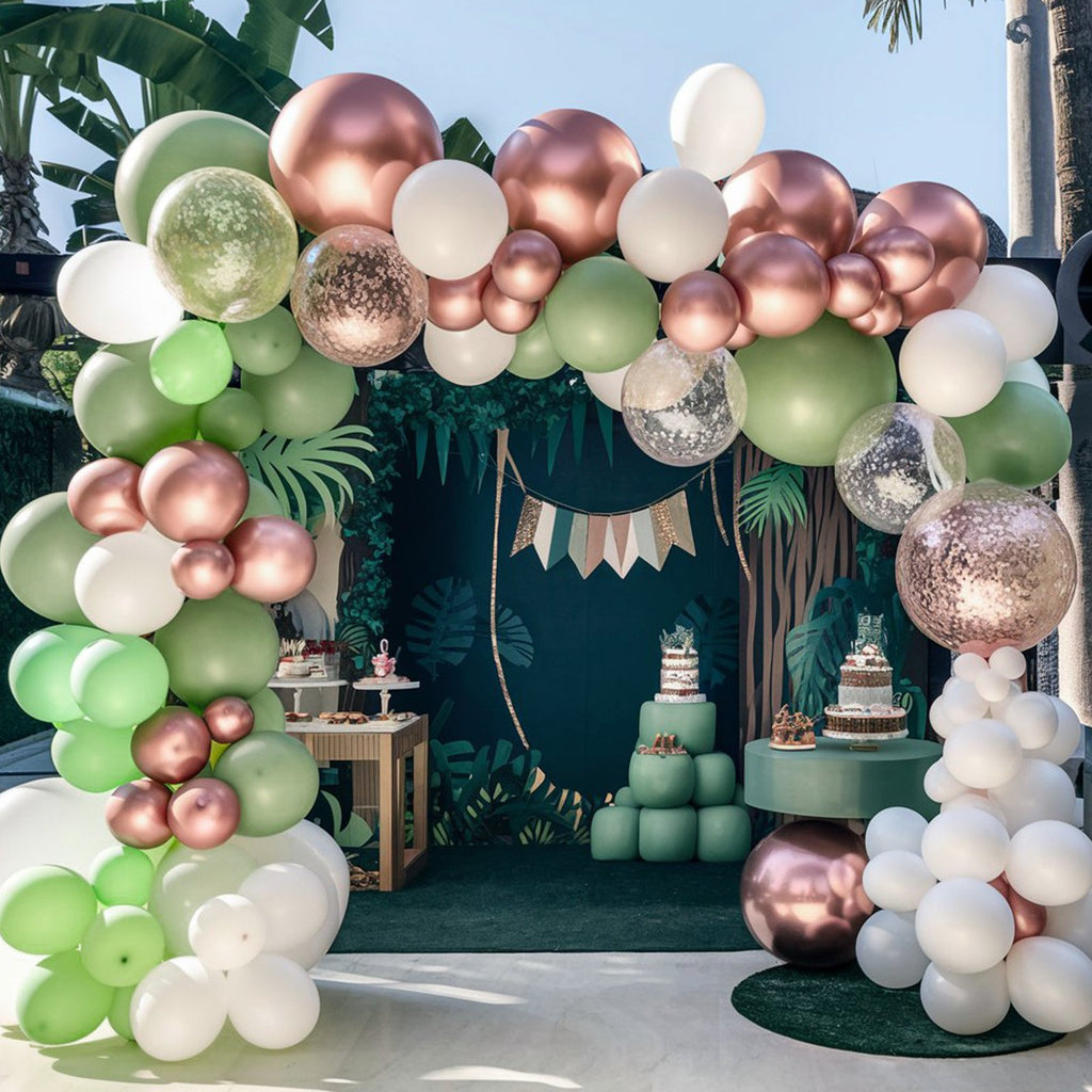 Jungle-themed party setup with balloon arches, cakes, and dessert tables.