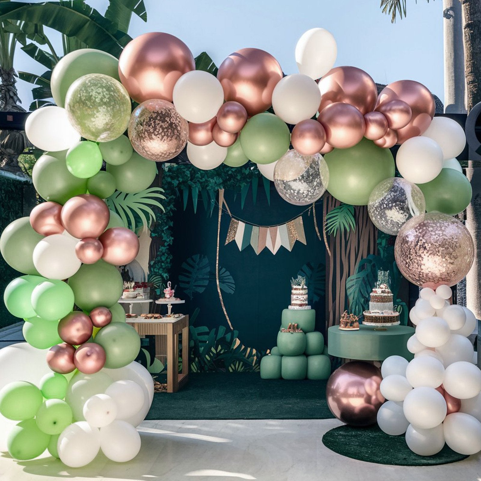 Jungle-themed party setup with balloon arches, cakes, and dessert tables.