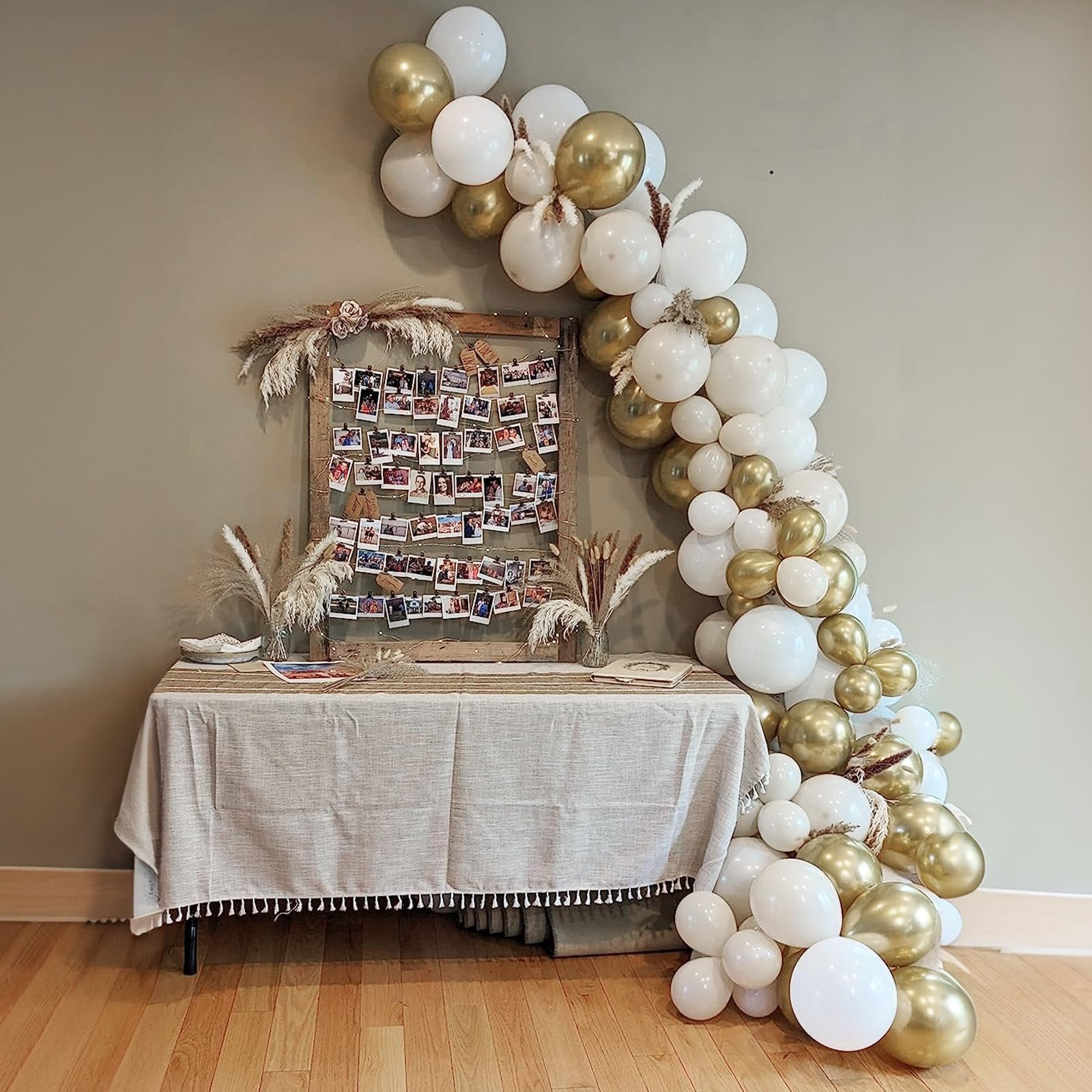 Balloon arch in white and gold with a table display of photos and decor