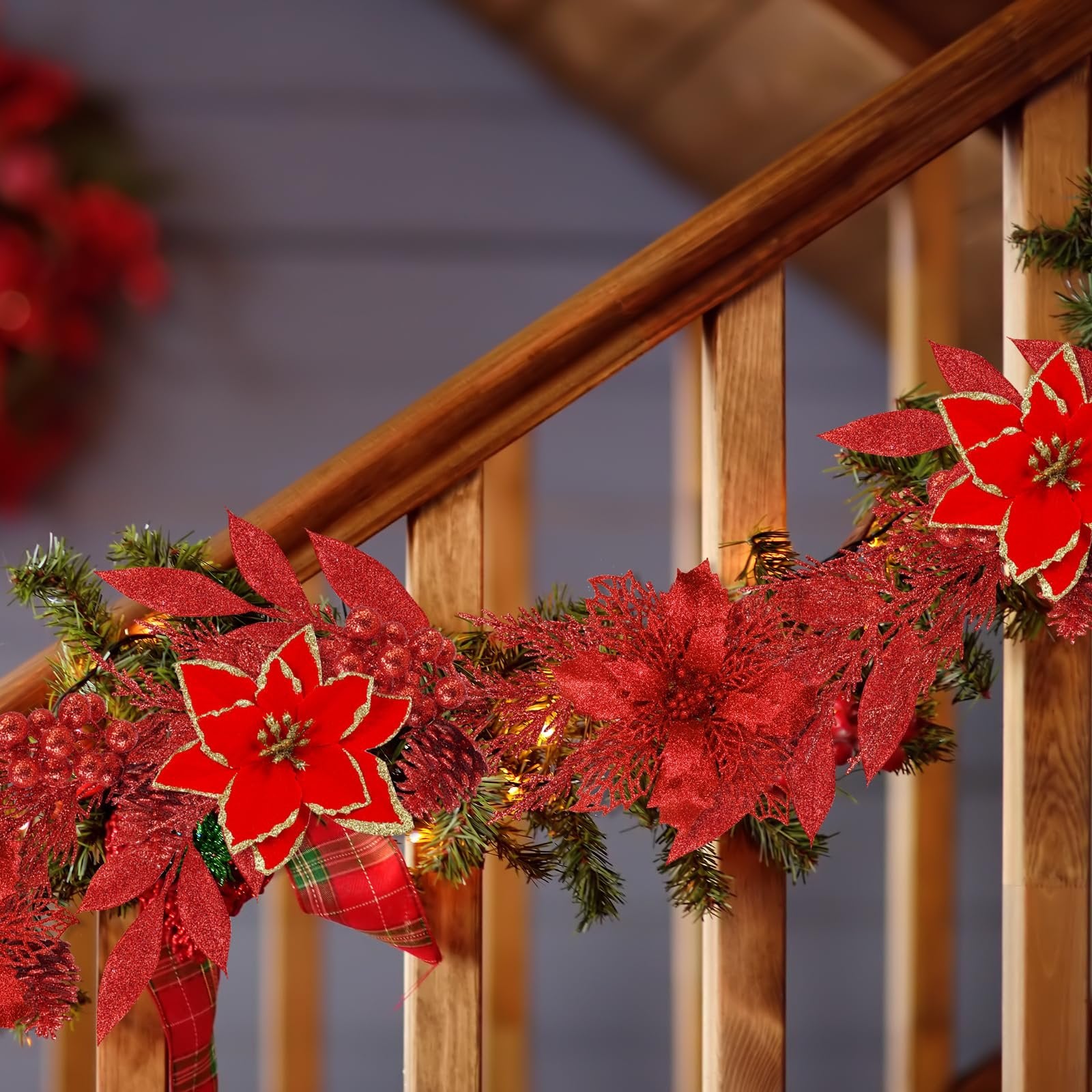Red glitter poinsettia garland with pine branches and lights draped on a wooden banister