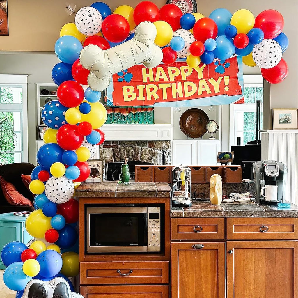 Birthday balloon arch with a bone-shaped balloon and a 'Happy Birthday!' banner, set up in a kitchen.