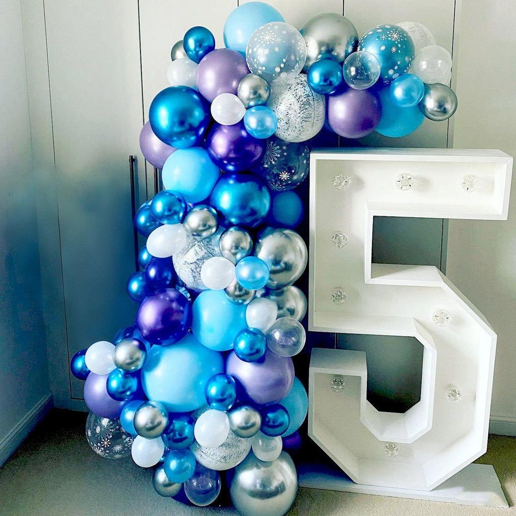Balloon arrangement in shades of blue, purple, and silver next to a large white marquee number 5.