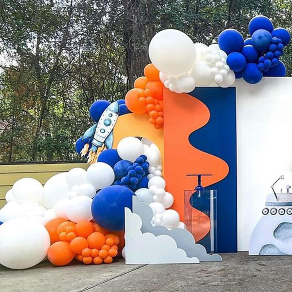 Balloon arch with white, blue, orange, and gold balloons, featuring a rocket and robot decoration, set outdoors.