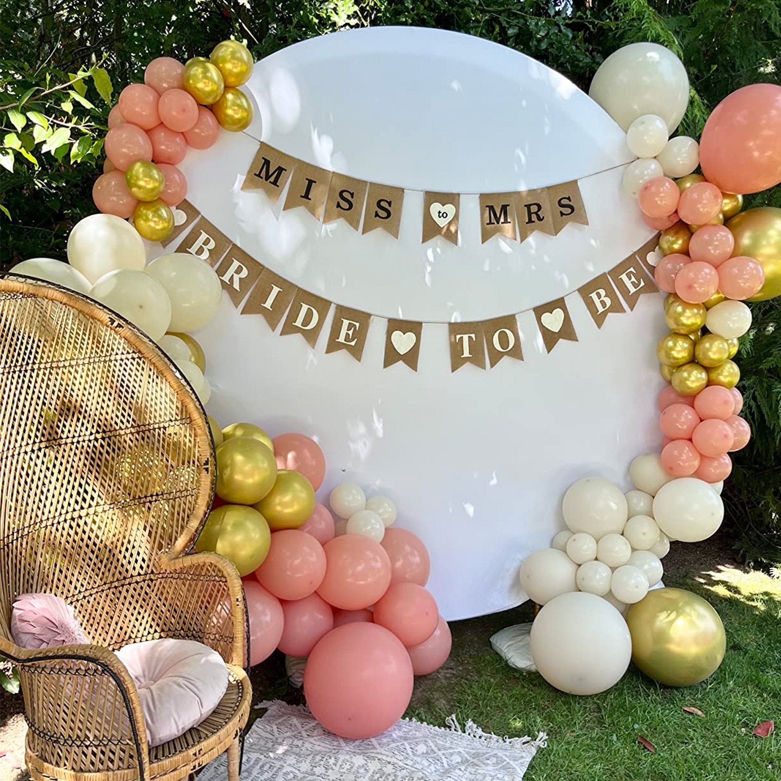 Bridal shower backdrop with balloons and a 'Miss to Mrs Bride to Be' banner, featuring a wicker chair.