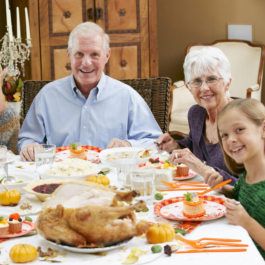 Family enjoying a Thanksgiving dinner with a roasted turkey, mashed potatoes, cranberry sauce, and desserts on a table set with festive plates and orange cutlery.