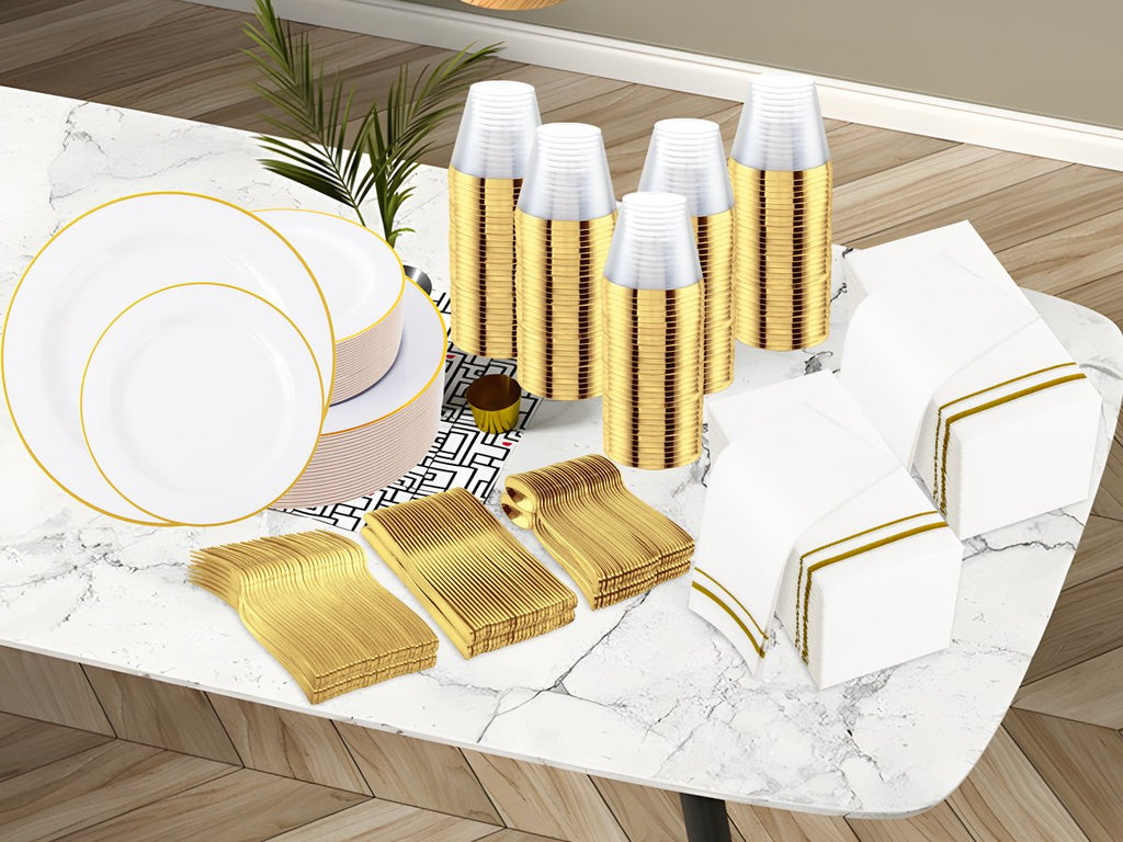 White and gold disposable dinnerware set including plates, cups, napkins, and cutlery arranged on a marble table.