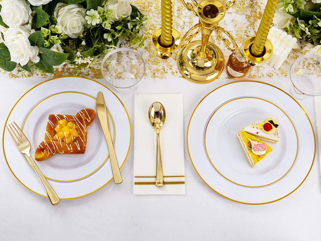 Table setting with white and gold disposable plates, cutlery, and napkins, featuring desserts and floral decor.