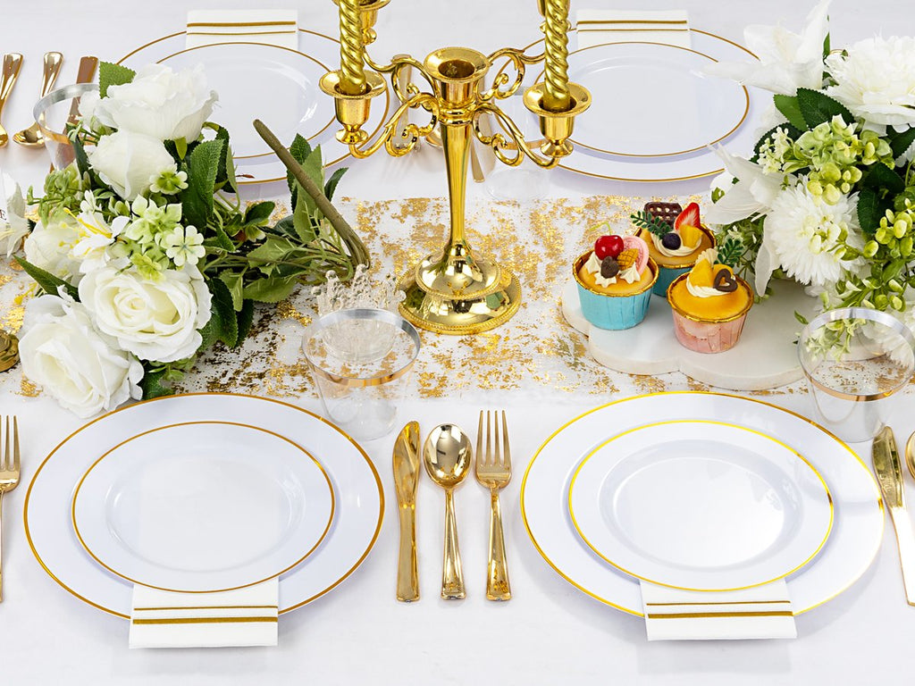Table setting with white and gold disposable plates, cutlery, cups, and napkins for a party.