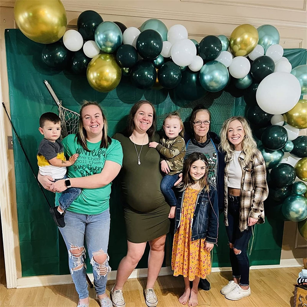 Family posing for a photo in front of a dark green backdrop with a balloon arch in dark green, gold, and white.