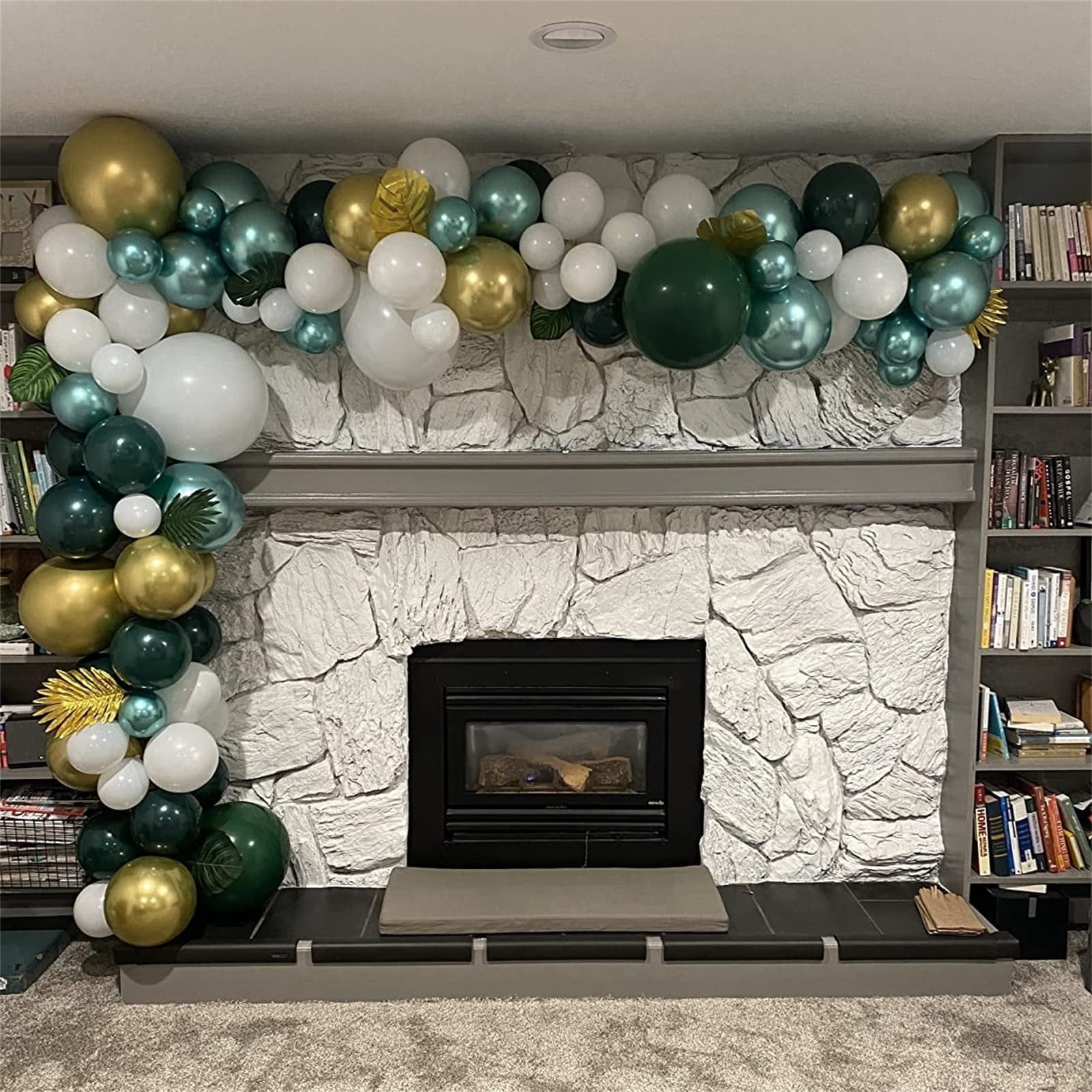 Balloon garland in dark green, gold, and white draped over a stone fireplace mantel