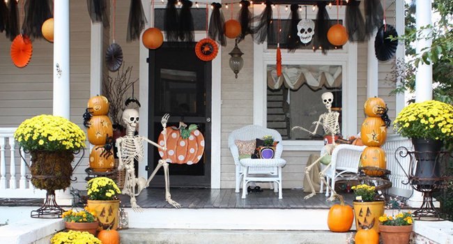 Halloween porch decoration with two skeletons, pumpkins, mums, and festive banners
