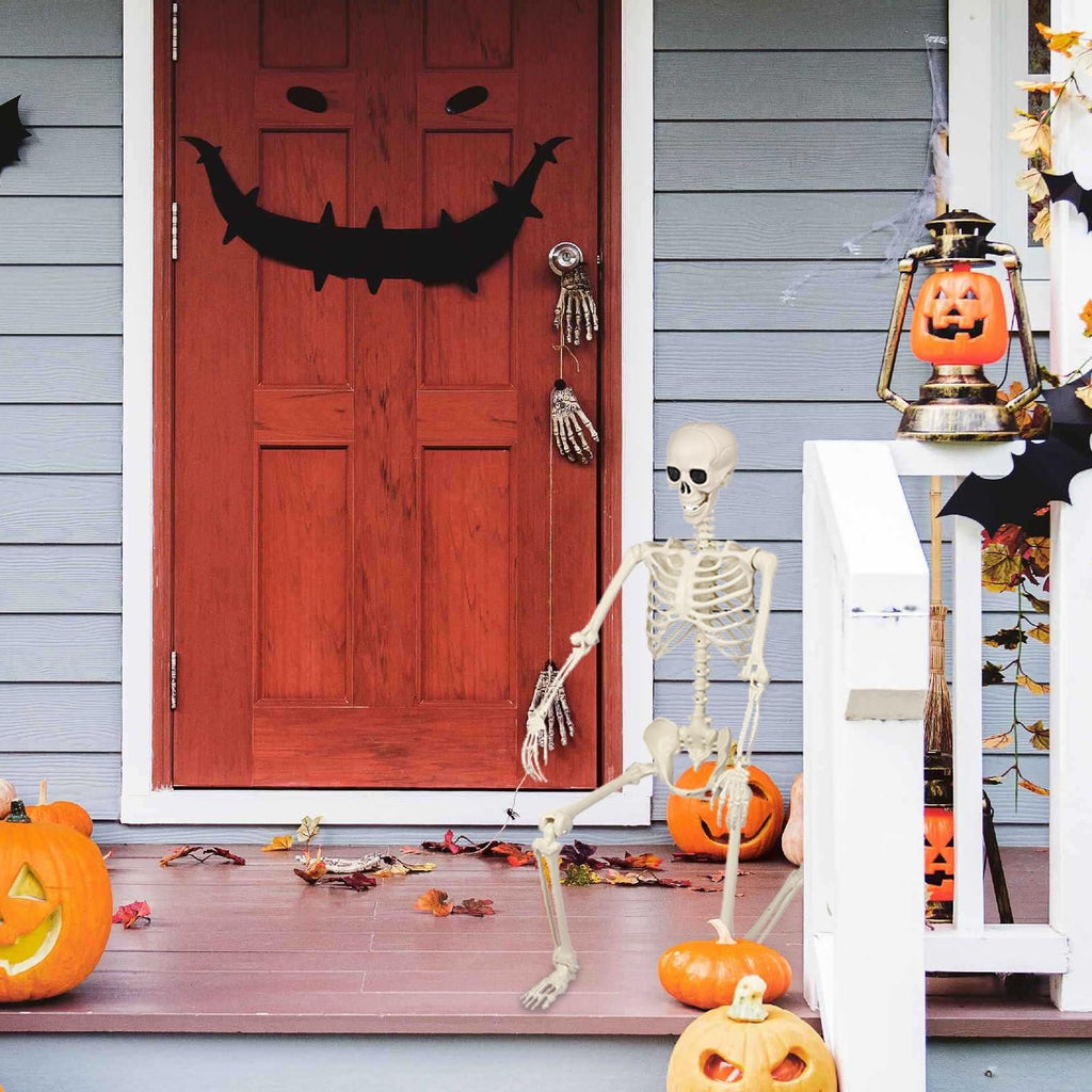 Halloween porch decoration with a poseable skeleton, jack-o'-lanterns, and bats on a red door and porch railing.