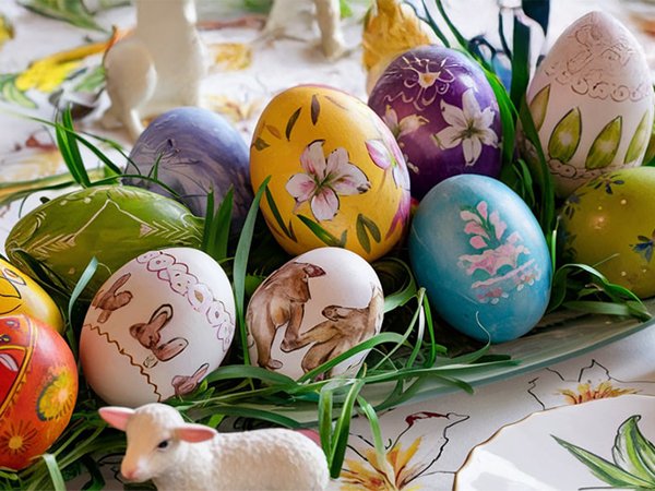 Decorated Easter eggs with various designs, including bunnies, bears, and floral patterns, arranged with grass and a lamb figurine.