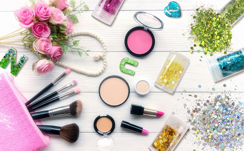 Flat lay of makeup products and glitter jars with pink roses and pearls on a white wooden background