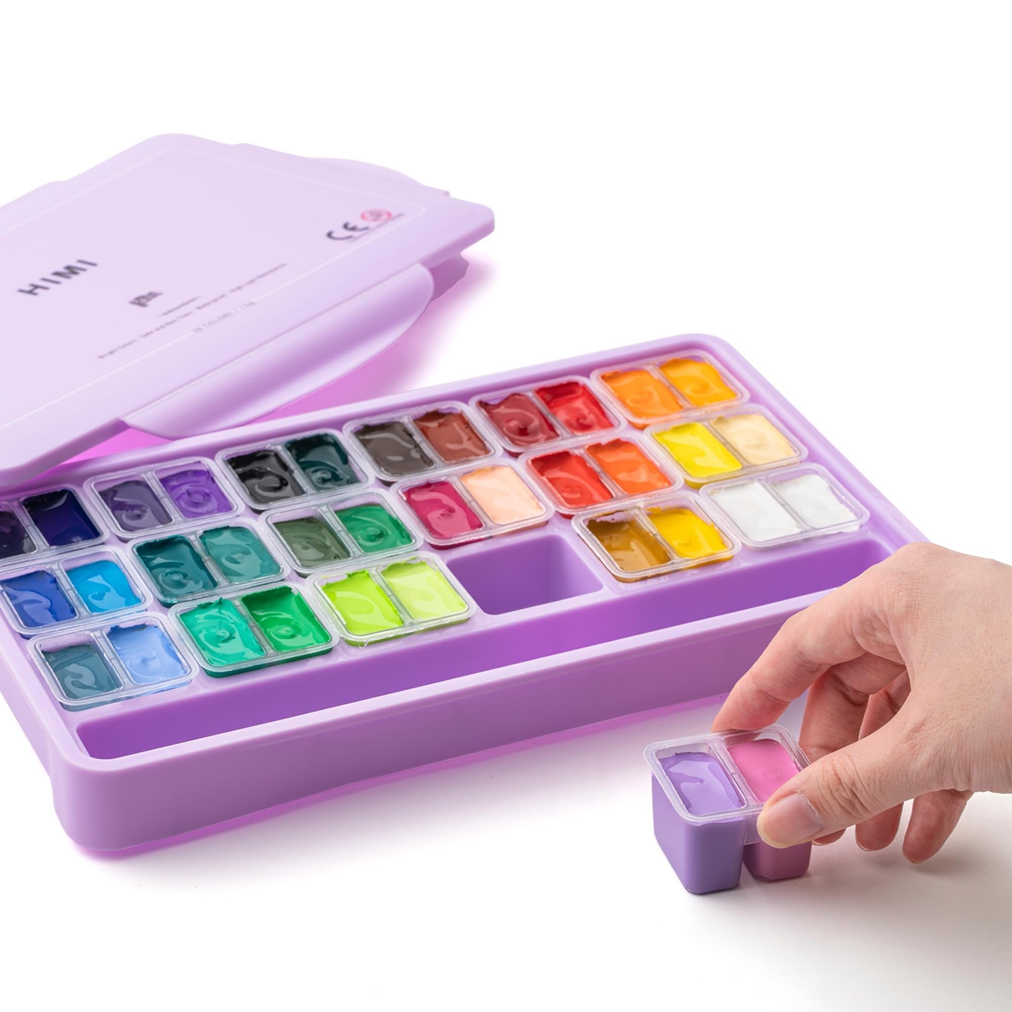 Open purple case of 36 jelly gouache paint cups with a hand holding two cups of purple and pink paint.