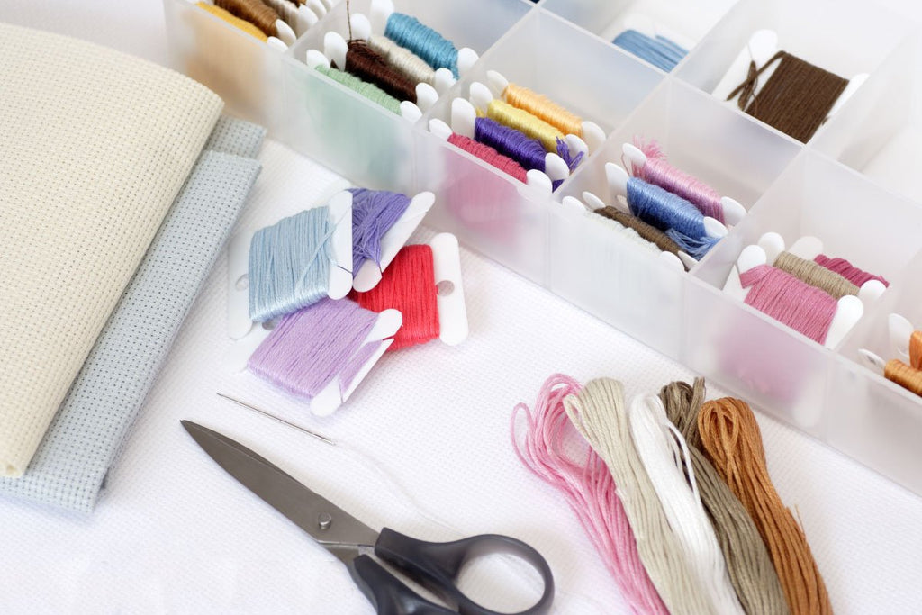 Embroidery floss organizer box filled with colorful threads, fabric, scissors, and a needle on a white surface.
