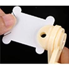 Close-up of a hand holding a white plastic bobbin winder with a cream-colored winding mechanism against a black background.