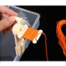 Hand using a plastic winder to wrap orange embroidery floss onto a white bobbin, with a clear organizer box in the background.