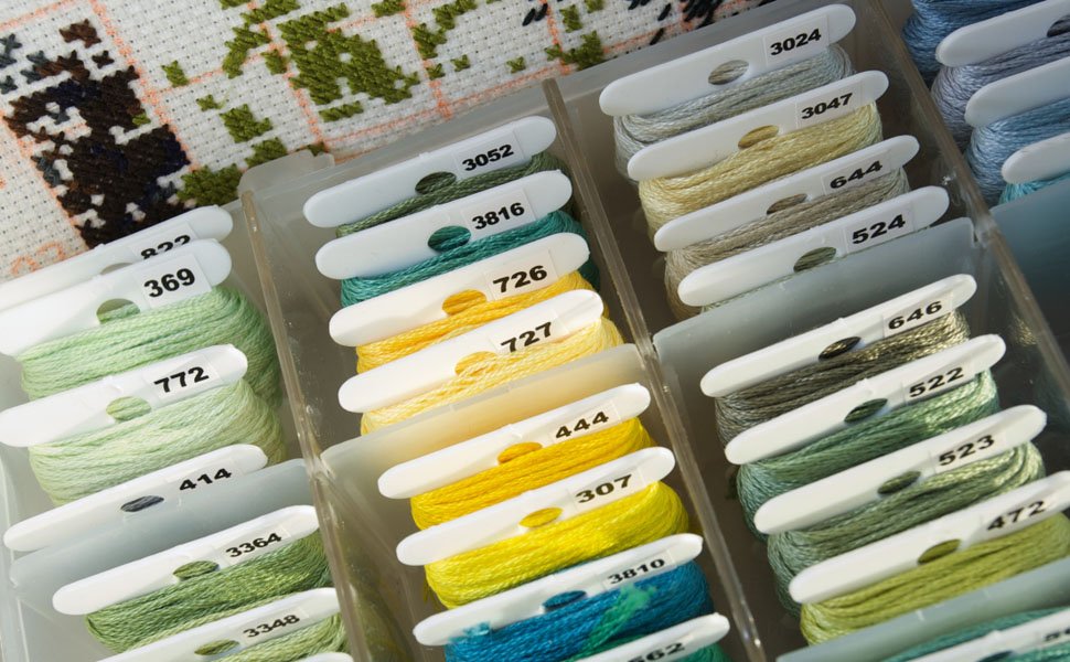 Embroidery floss organizer box filled with bobbins wound with colorful threads, with a cross-stitch fabric in the background.