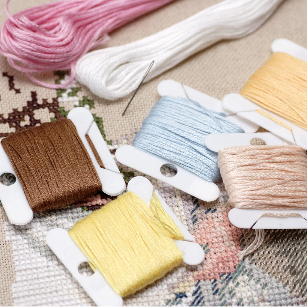 Embroidery floss in various colors wound on plastic bobbins, with a needle and fabric in the background.