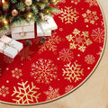 Red Christmas tree skirt with gold snowflake print, shown under a decorated tree with gifts and pinecones.