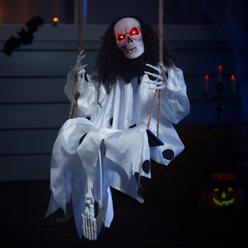 Hanging clown skeleton prop with glowing red eyes and white tattered costume, sitting on a swing in a dark, spooky setting.