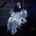 Hanging clown skeleton prop with glowing red eyes and white tattered costume, sitting on a swing in a dark, spooky setting.