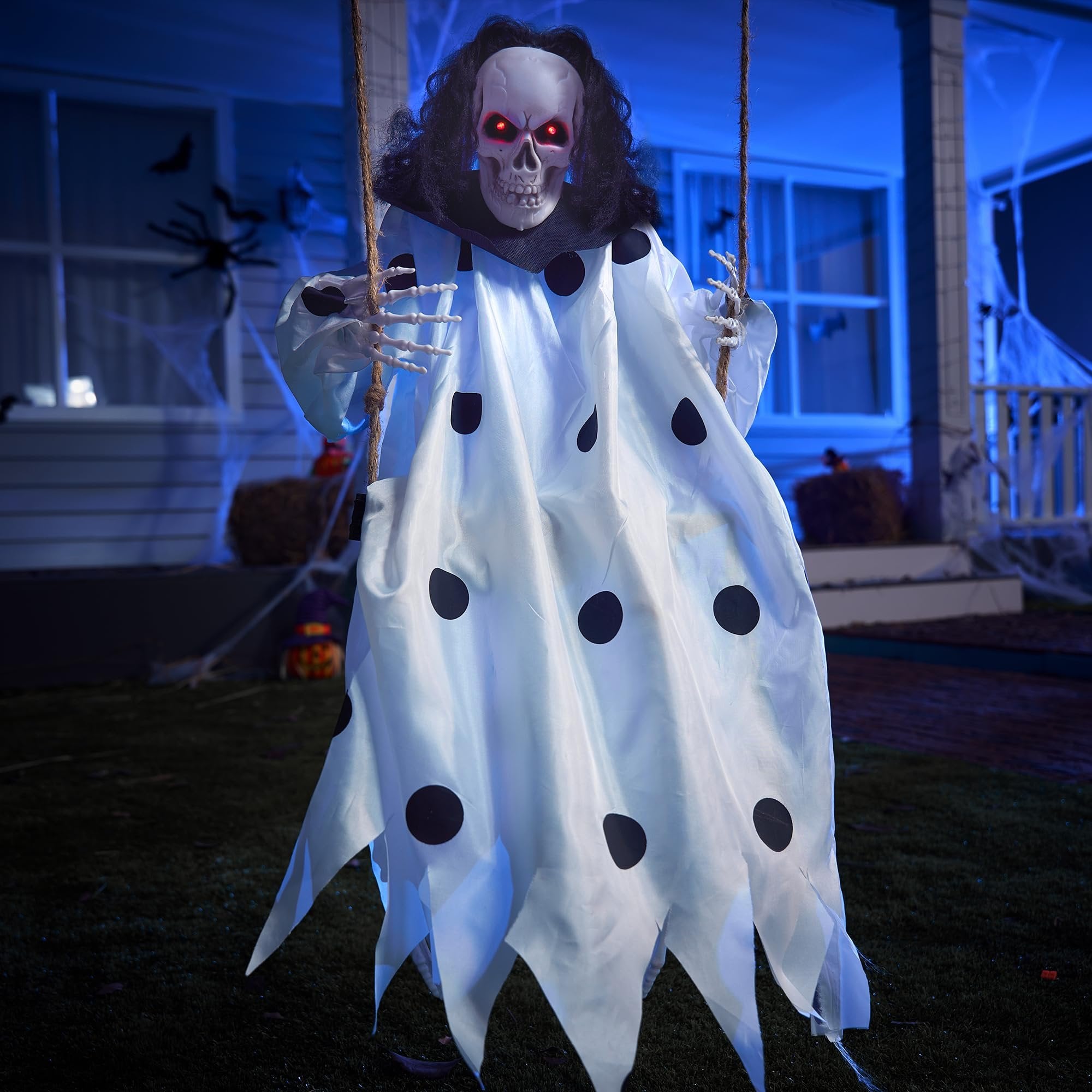 Hanging clown skeleton Halloween decoration with red glowing eyes and a white polka dot costume, swinging from rope outdoors at night.