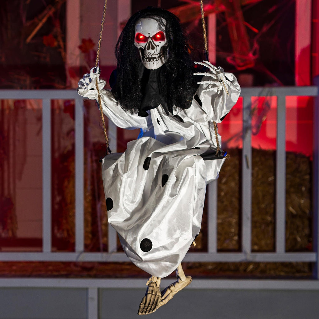 Hanging clown skeleton prop with glowing red eyes and black hair, wearing a white dress with black polka dots, sitting on a swing.