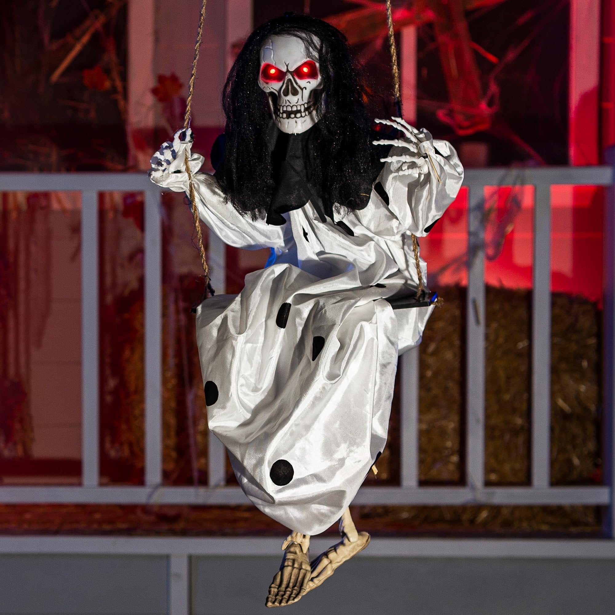 Hanging clown skeleton prop with glowing red eyes and black hair, wearing a white dress with black polka dots, sitting on a swing.