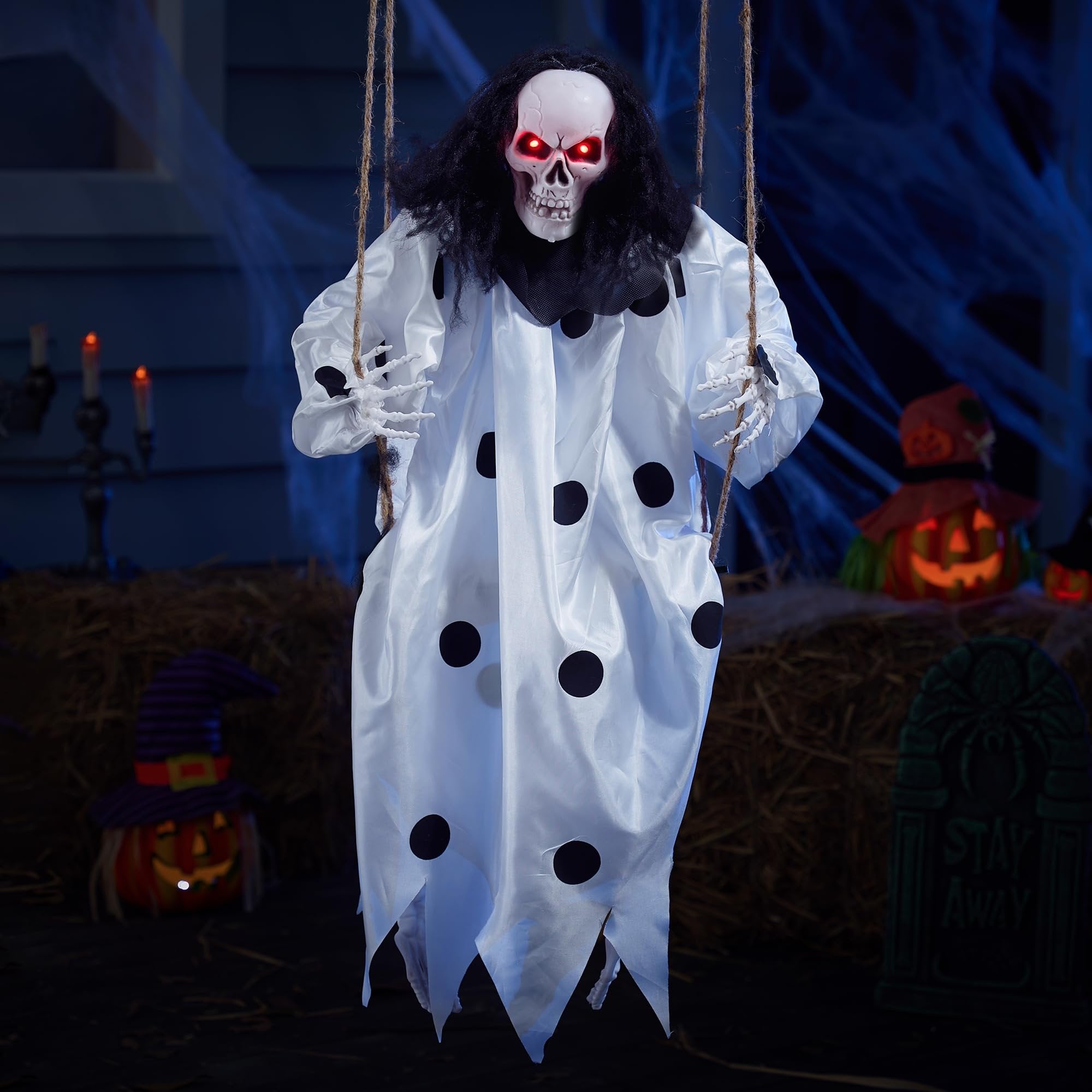 Hanging clown skeleton decoration with red glowing eyes and black polka dots on white costume, swinging on ropes.