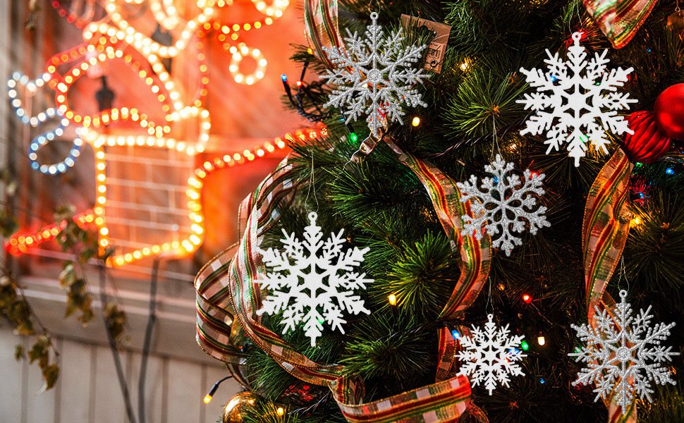 Silver glitter snowflake ornaments hanging on a Christmas tree with festive ribbon and lights.