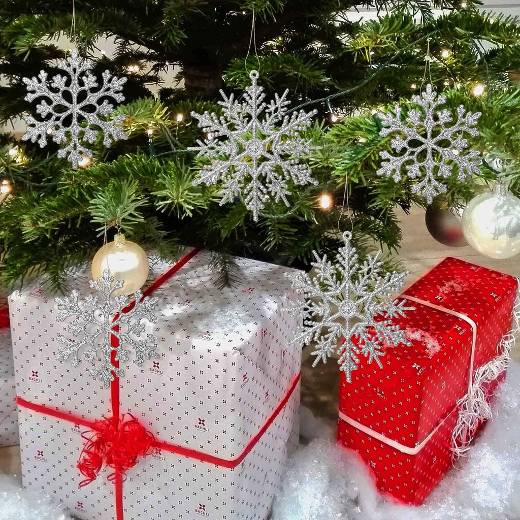 Silver glitter snowflake ornaments hanging on a Christmas tree above wrapped gifts