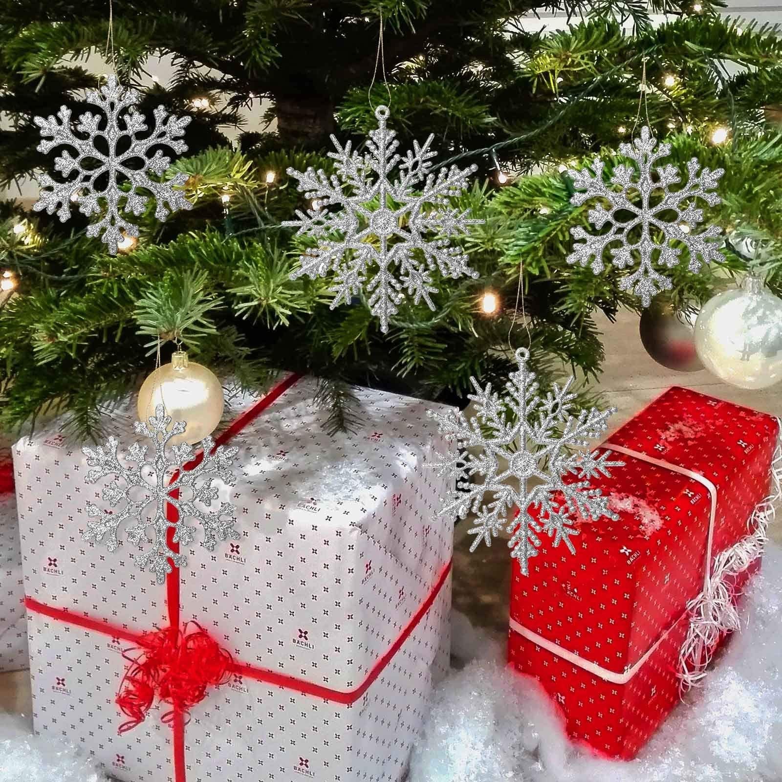 Silver glitter snowflake ornaments hanging on a Christmas tree above wrapped gifts
