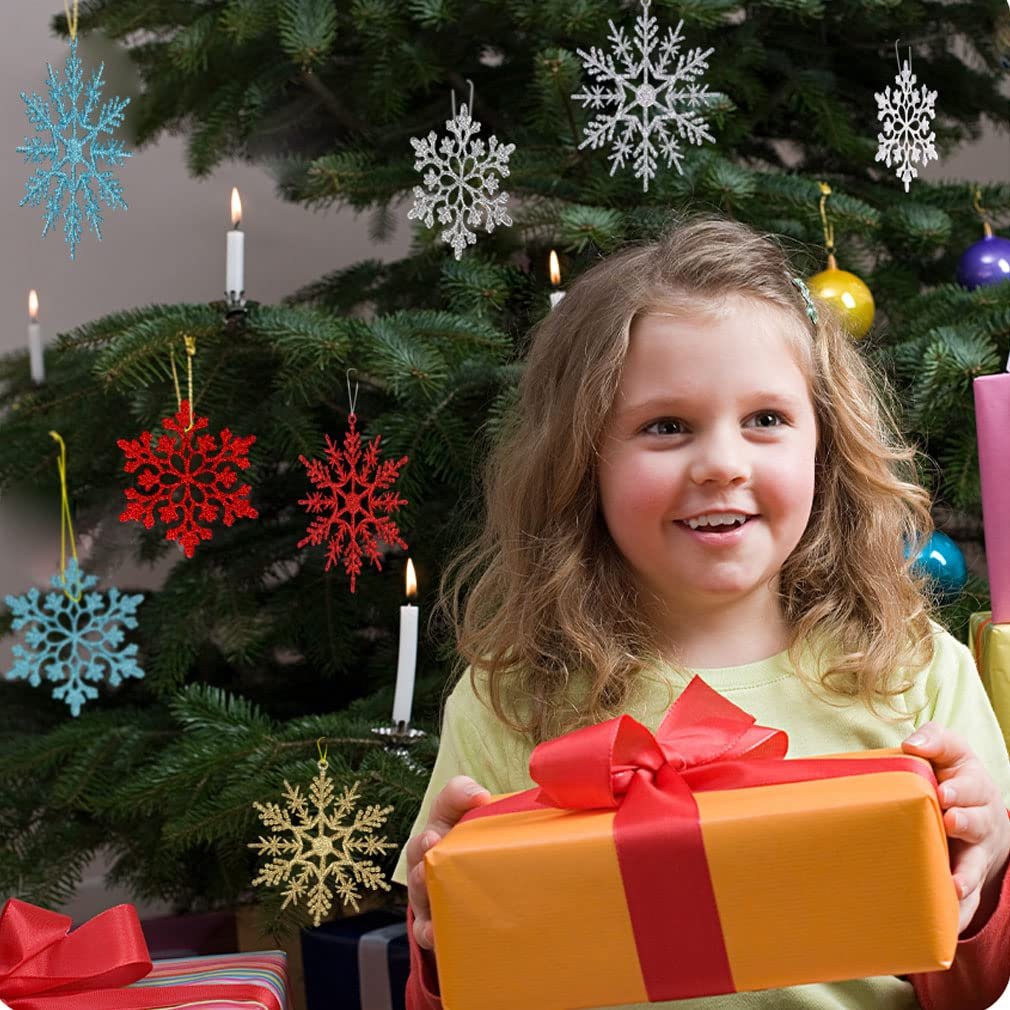 Smiling girl holding an orange gift with a red ribbon in front of a decorated Christmas tree with snowflake ornaments