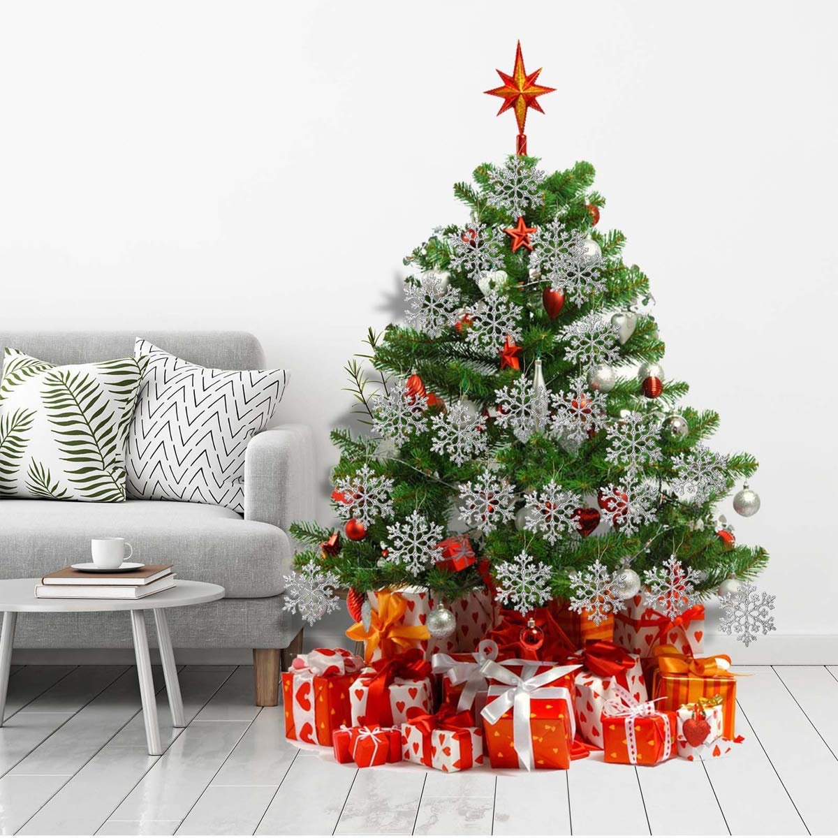 Christmas tree decorated with silver glitter snowflake ornaments and red baubles, surrounded by wrapped gifts.
