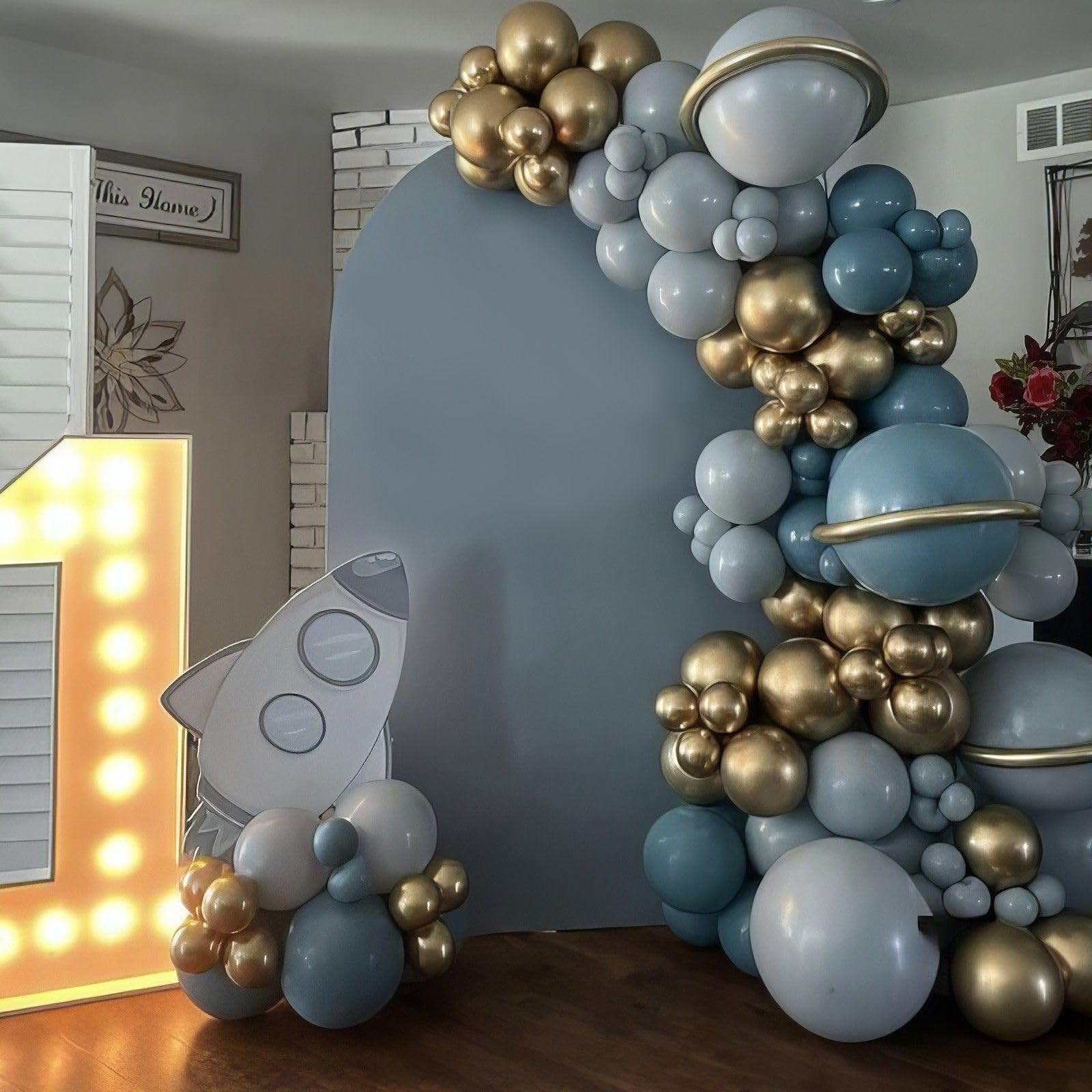 Balloon arch with dusty blue, sage green, retro sea blue, sand white, and metallic gold balloons, featuring a rocket cutout and a light-up number 1.